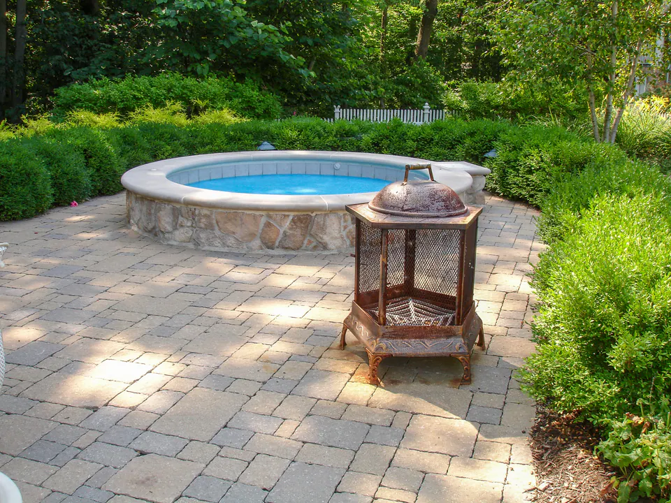 Raised round spa with natural stone wall, concrete paver patio, and surrounding hedge planting